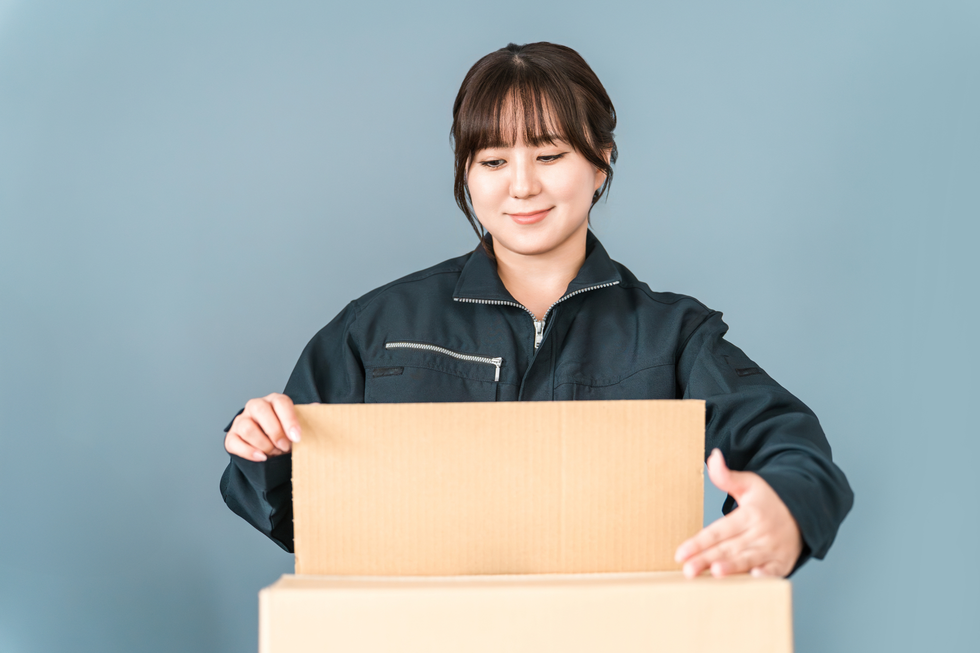 ダンボールを開く作業着姿の女性